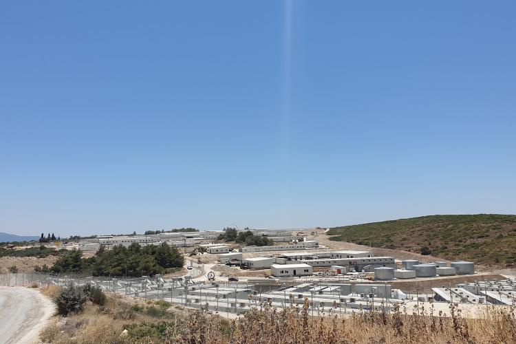 Un gran complejo con múltiples edificios industriales y tanques bajo un cielo azul despejado, enclavado cerca de la frontera europea. Rodeado de colinas y escasa vegetación, es un testimonio de la industria moderna y de la evolución de las políticas fronterizas europeas. | Jacob Warn